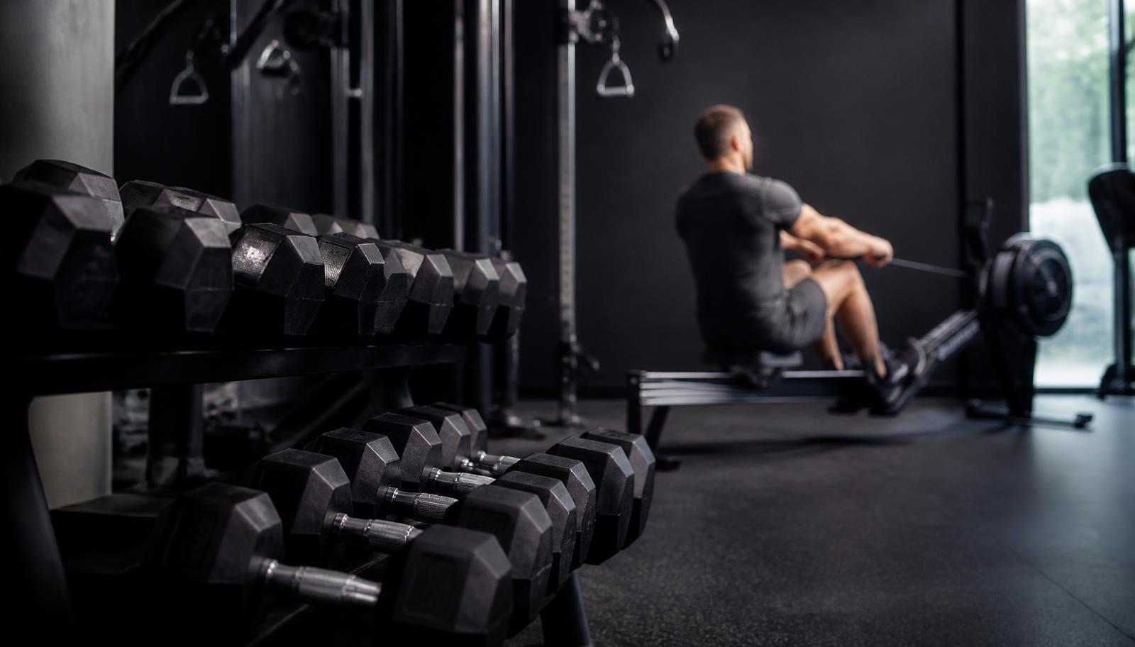 Manubri in primo piano e vogatore sullo sfondo: allenamento per perdere grasso che unisce pesi e cardio